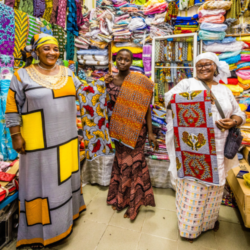 Maimouna Dougan (links), Kundin des Oikocredit-Partners Fin'Elle, mit ihrer Tochter und Schwester in ihrem Stoffladen in Côte d’Ivoire.